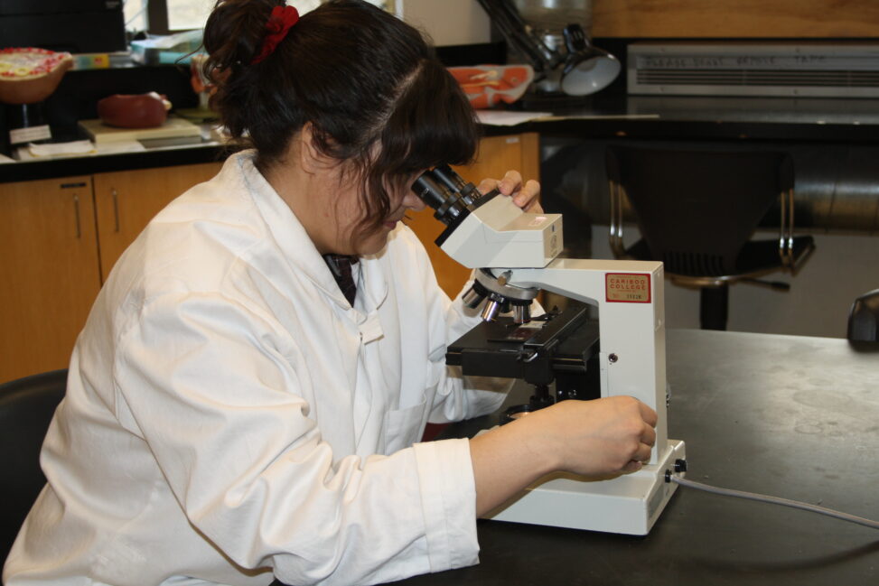 Indigenous student in an biology lab with a microscope.