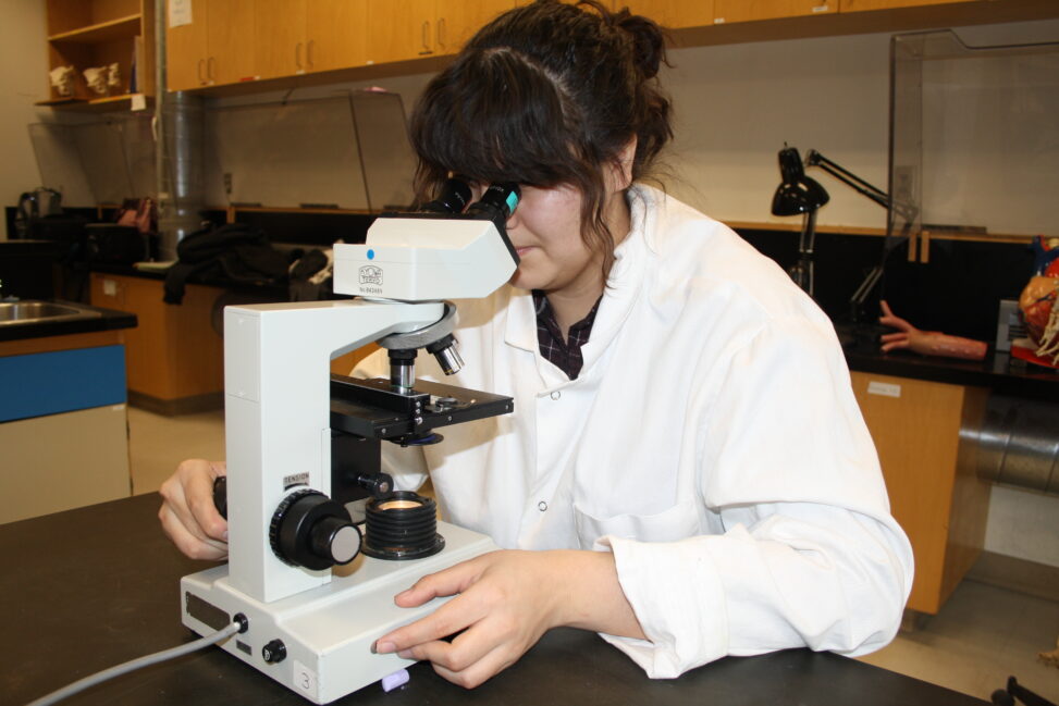 Indigenous student in a biology lab using a microscope.