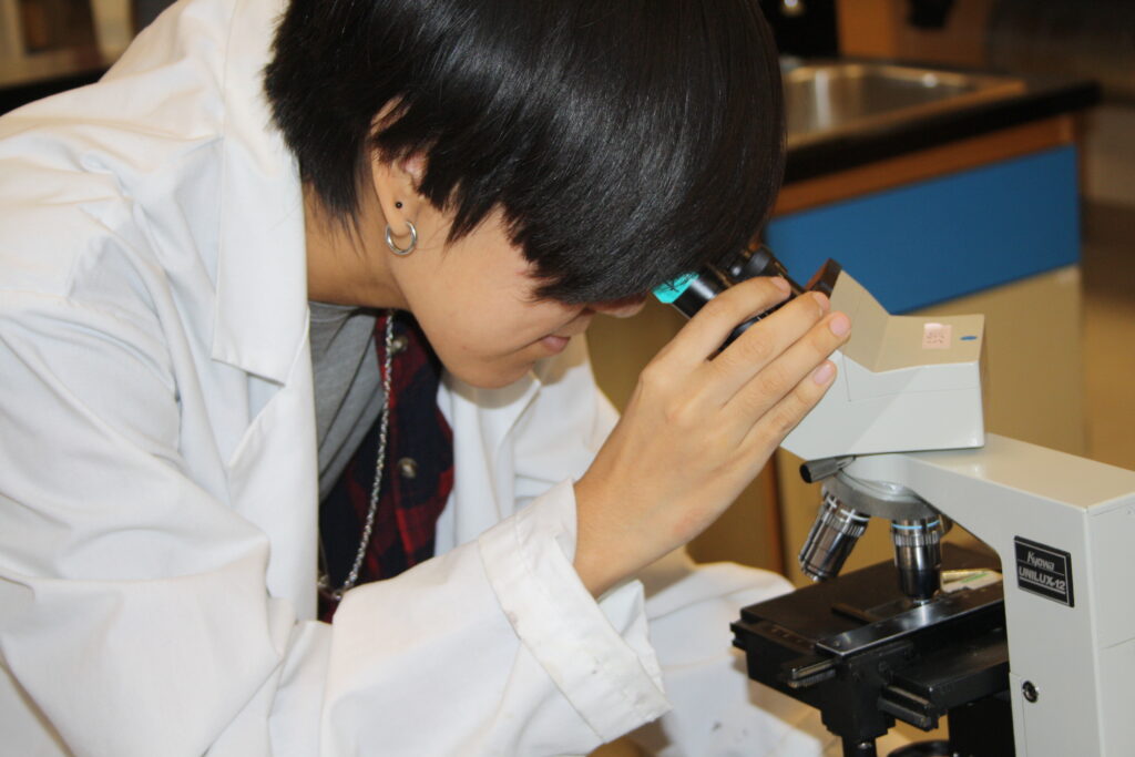 Indigenous student in a biology lab with a microscope.
