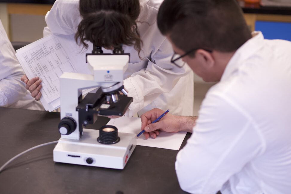 ndigenous students in a biology lab working around a microscope.
